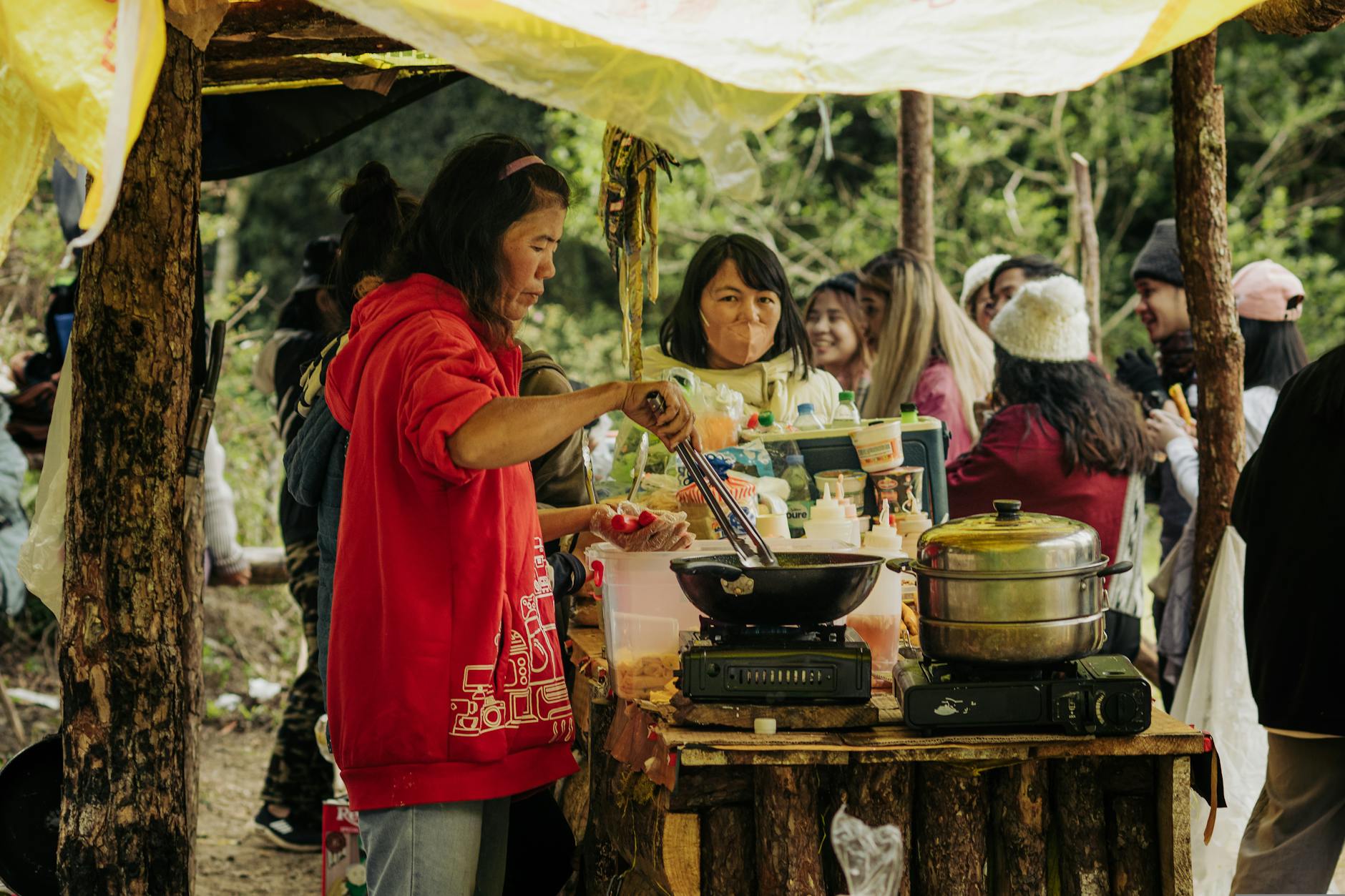 Women preparing street food at an outdoor market, bustling with people and vibrant activities.