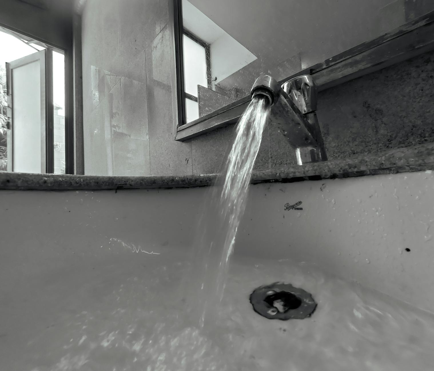 Monochrome close-up of water flowing from a faucet into a sink with selective focus.