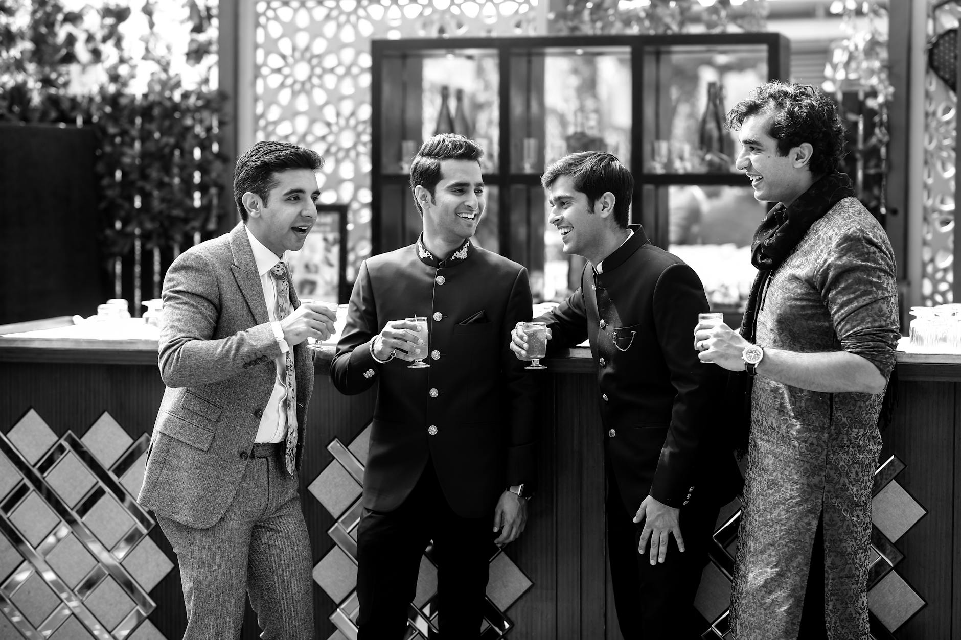Four men in formal attire enjoying drinks and conversation in a social setting.