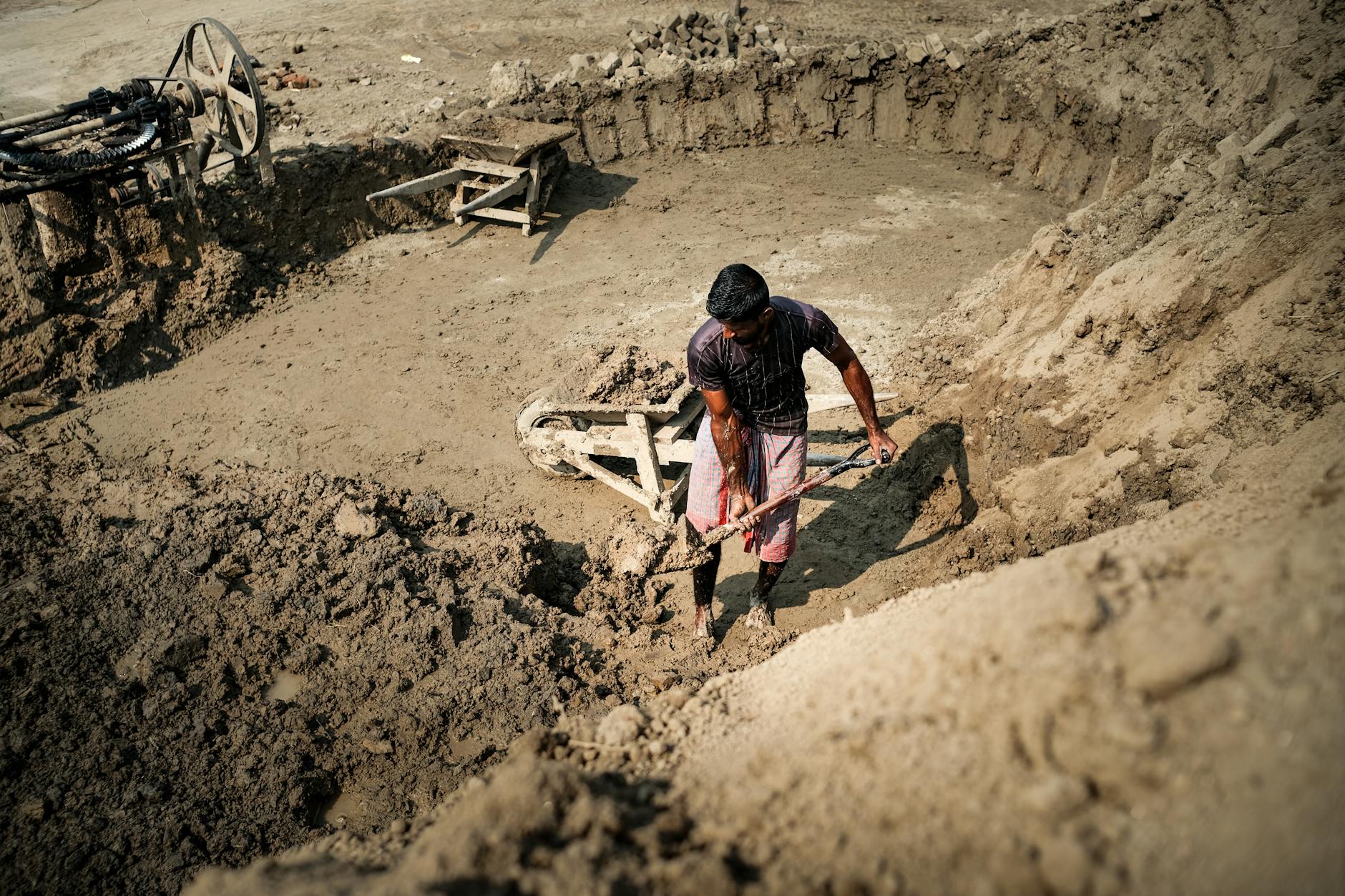 A worker digs in a construction site pit, showcasing manual labor and industry.