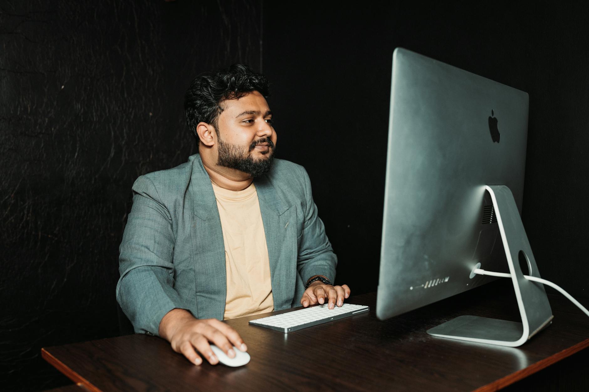 An adult male in a suit working on a desktop computer in a sleek office environment.