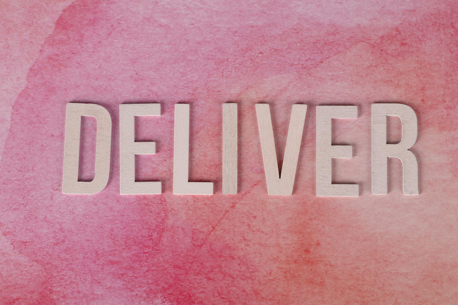 Wooden letters spelling 'Deliver' on a pink textured background for business concept.