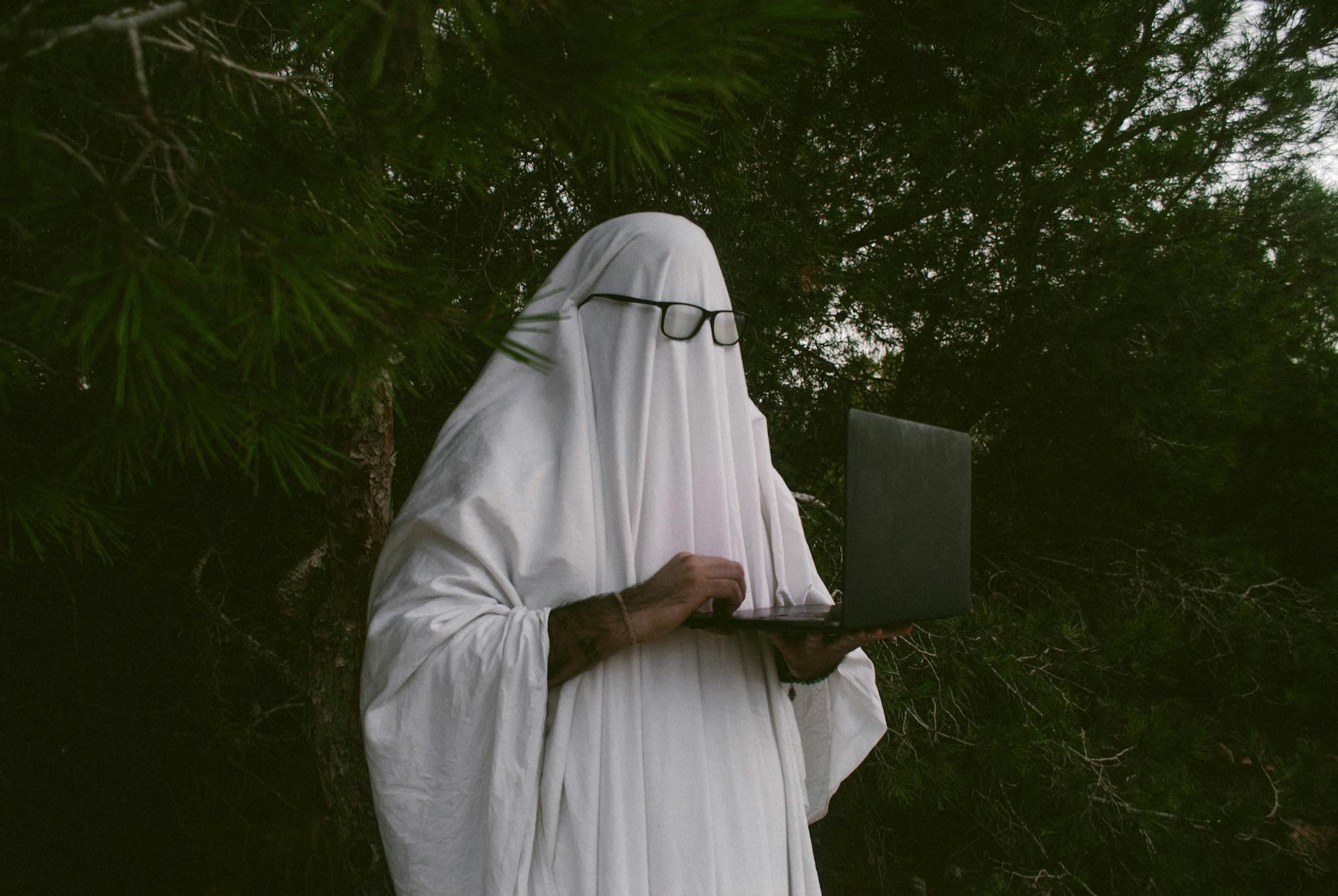 Ghostly figure with glasses using a laptop in a humorous outdoor setting.