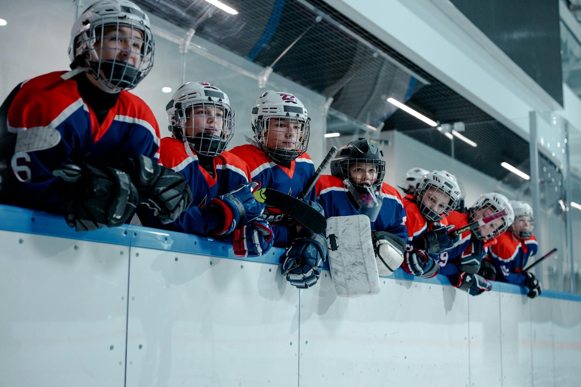 A junior ice hockey team waits eagerly at the rink edge, embodying teamwork and anticipation.