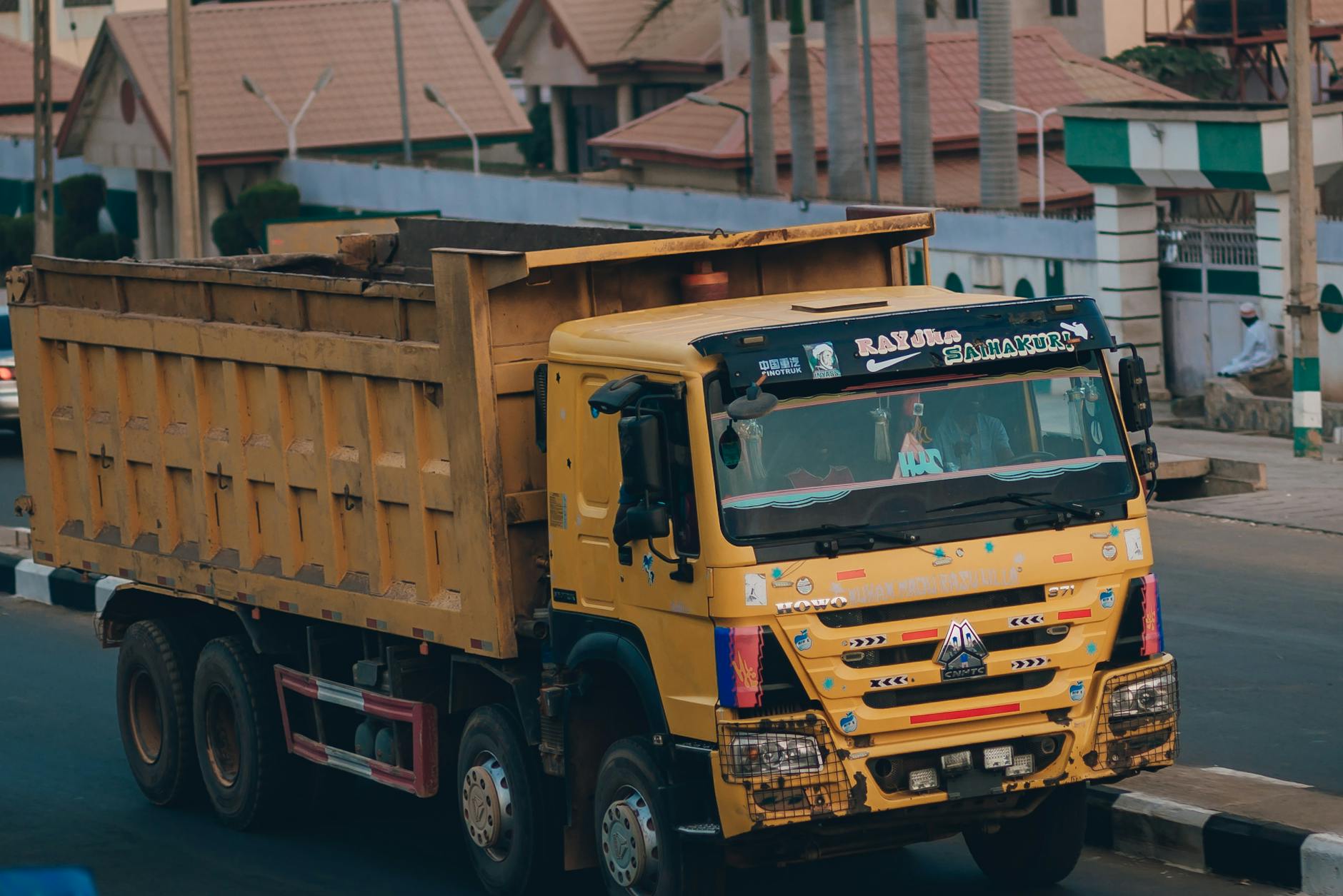 Large yellow dump truck driving through a city street in an urban setting.