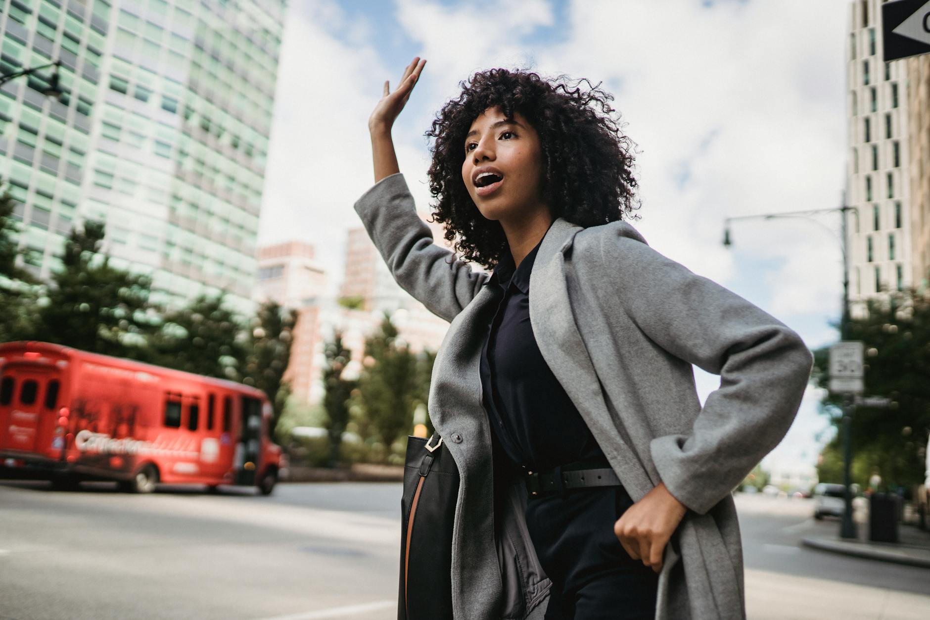 Young African American female with Afro hairstyle waving hand on city road while looking away