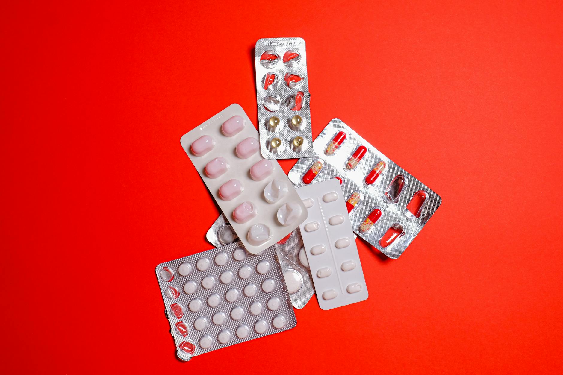 Blister packs with assorted pills over a vibrant red surface. Ideal for healthcare themes.