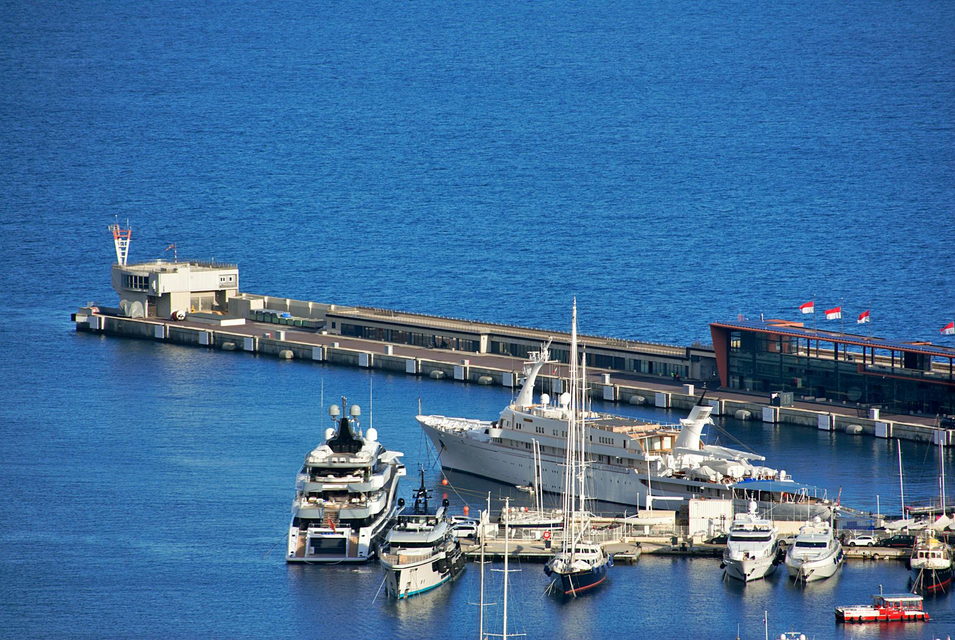 Aerial view of luxury yachts docked at the marina in Monaco with vibrant blue sea.