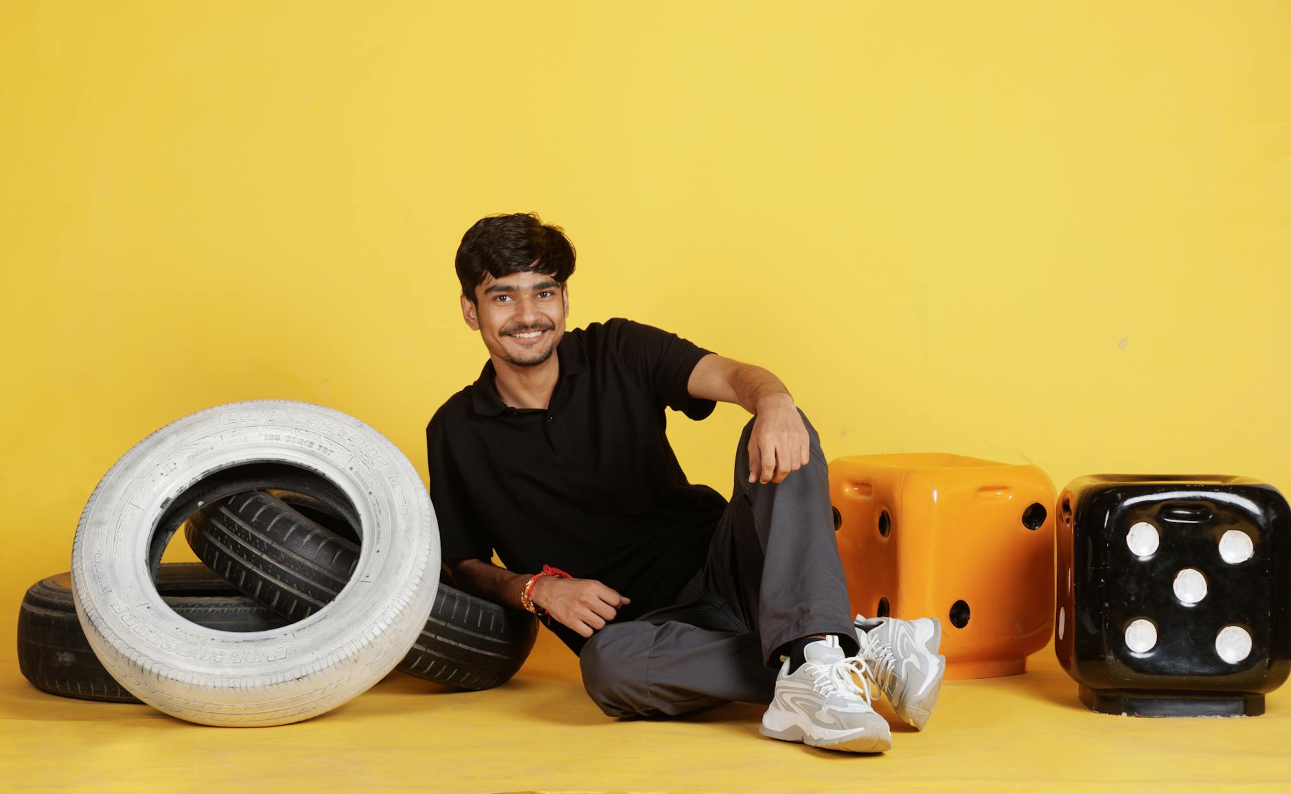 Cheerful man in casual wear posing with tires and oversized dice on yellow background.
