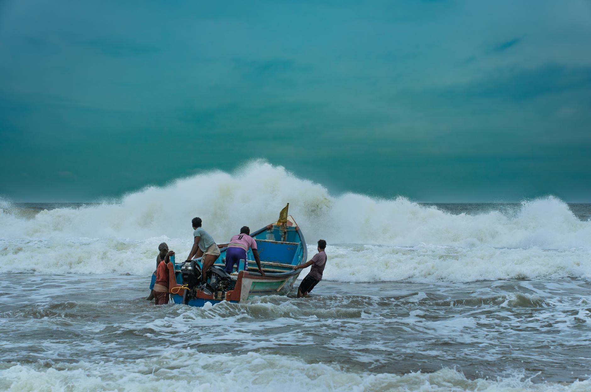 Fishermen pushing a boat through ocean waves on a cloudy day, capturing the essence of maritime adventure.