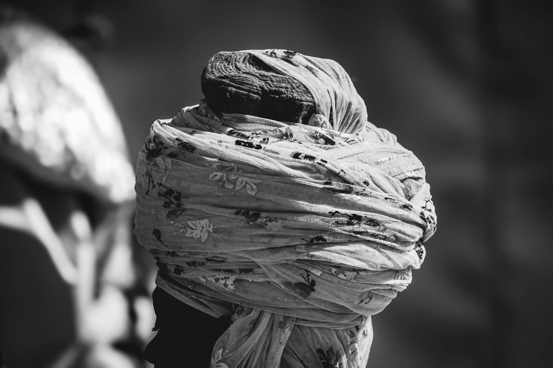 Black and white portrait of a person wrapped in patterned fabric, obscuring the face.