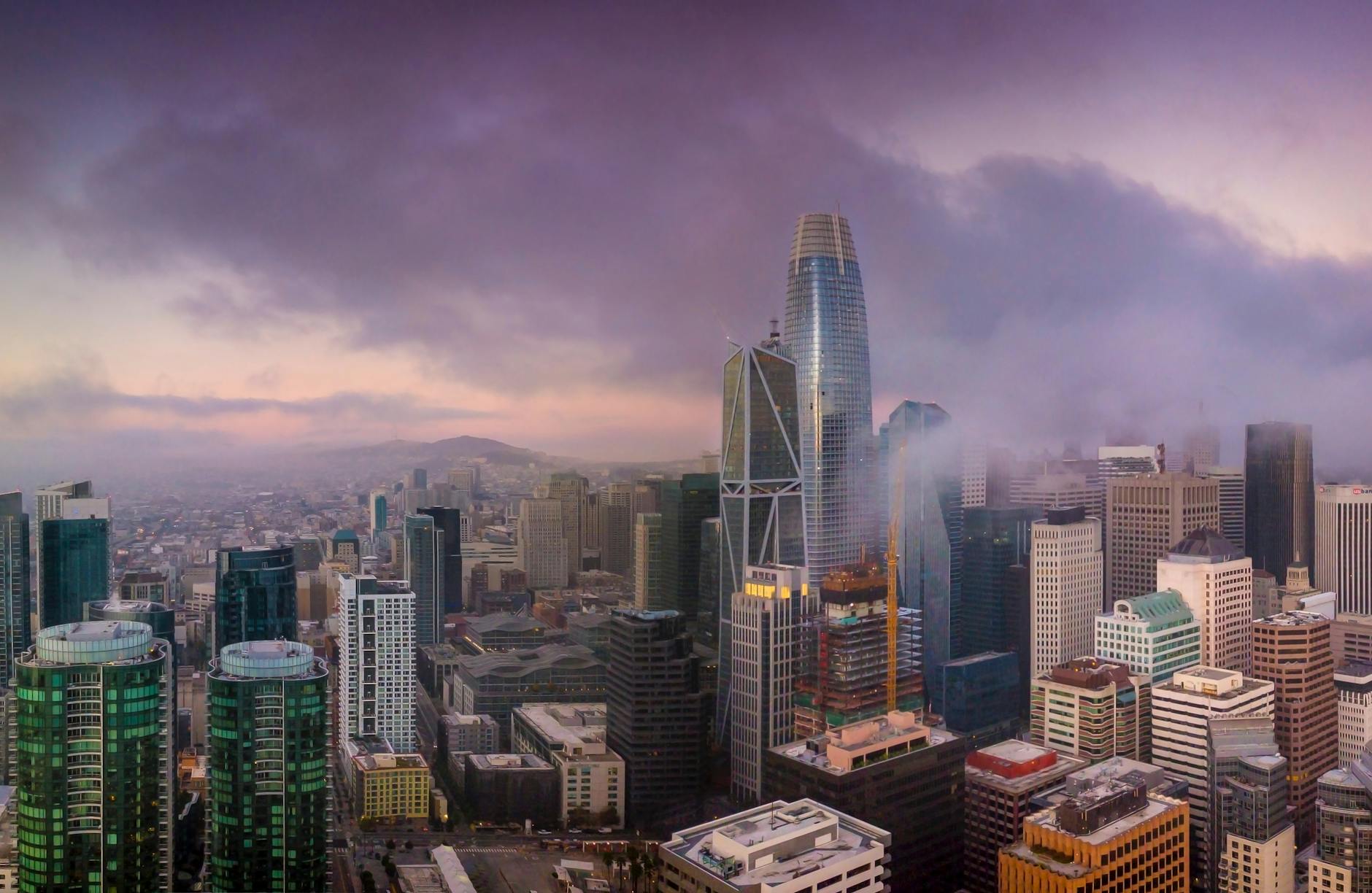Aerial view of San Francisco's skyline at sunset with iconic skyscrapers and dramatic clouds.