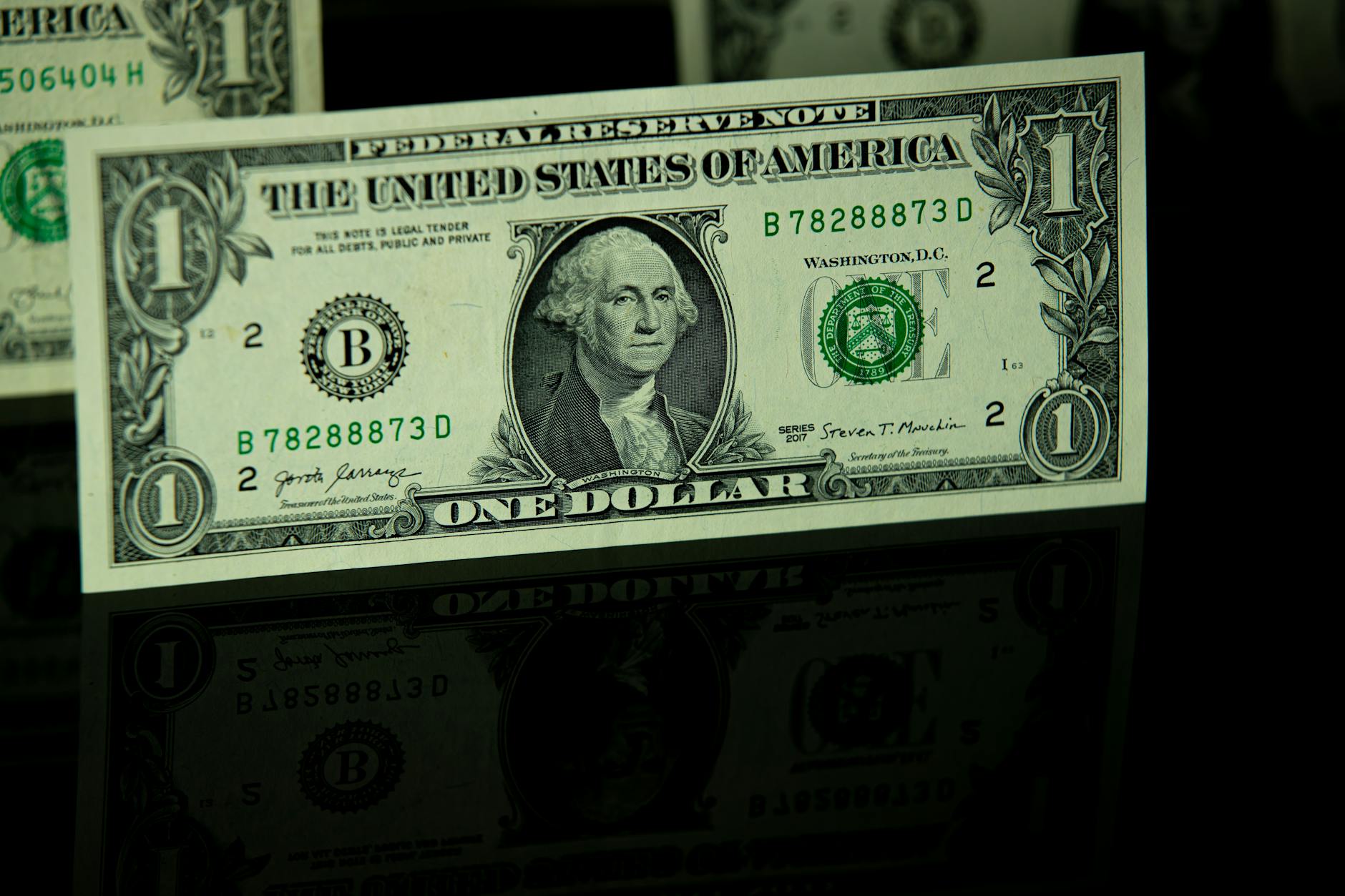 Detailed close-up of a US one-dollar bill with reflection, highlighting currency design.