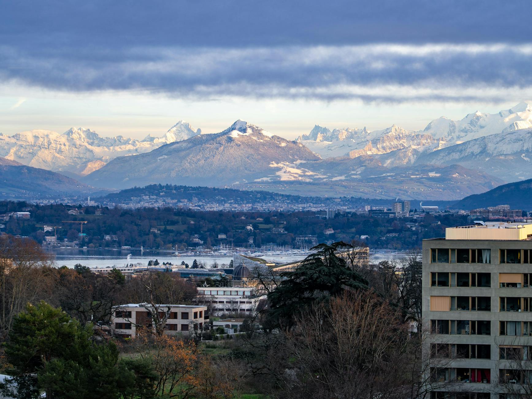 A breathtaking view of Geneva with Swiss Alps backdrop under a cloudy sky at day.