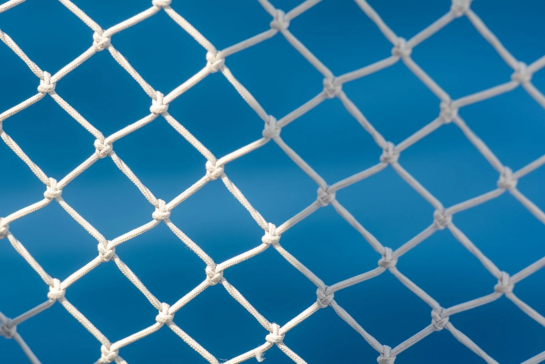 Close-up of a white mesh fence with blue background, creating a modern abstract pattern.